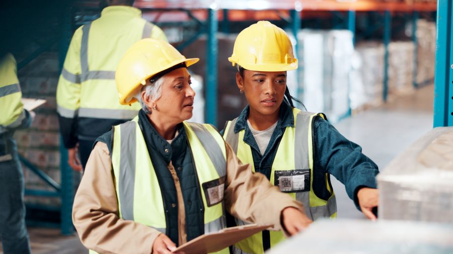 Deux femmes portant des casques de chantier jaunes inspectent des machines.